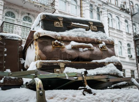 Foto de Maletas vintage cubiertas de nieve en el techo de un coche sobre el fondo de una antigua casa como concepto de viaje. - Imagen libre de derechos