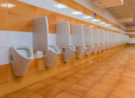 Photo for Long line of urinals in public toilet with white orange ceramic tiles - Royalty Free Image