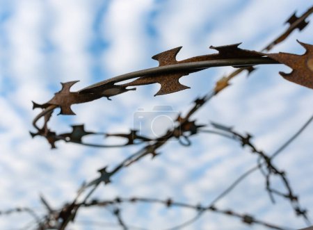 Extreme close-up of rusted barbed wire against a beautiful light cloudy sky