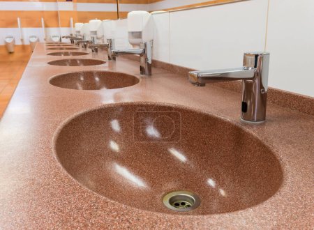 Reihe von Waschbecken mit automatischen Wasserhähnen und keramischen Waschbecken in einer öffentlichen Toilette