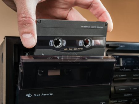 Téléchargez les photos : Une main d'homme tient une cassette audio sur le pont ouvert d'un magnétophone auto-inversé. - en image libre de droit