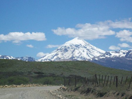 Curving dirt road in the mountains with a snow covered volcano in the background, showcasing a wonderful day to travel