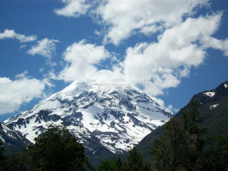 Volcano, snow peaked, covered by clouds and blue skies