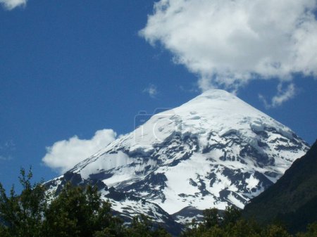 Monumental snow covered volcano with puffy white cloud above the visible peak