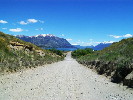 scenic route of dirt road that leads to a lake with mountain range in the background