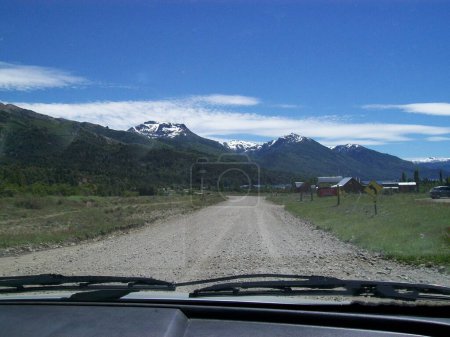 picturesque gravel road in remote area with some house at a distance and a mountain range in the background