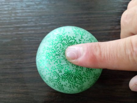 Photo for A person presses his finger on a soft green ball lying on a wooden surface. - Royalty Free Image