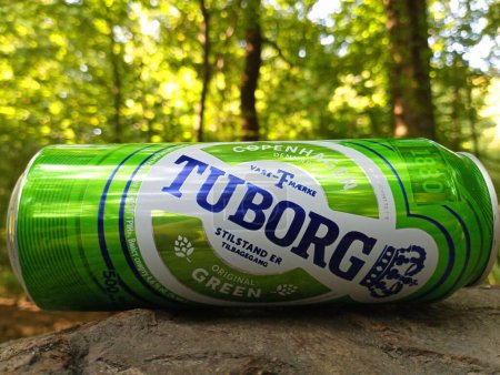 Foto de Aldea de Kornalovichi, distrito de Sambir, región de Lviv, Ucrania - 10 de septiembre de 2023: Una lata de metal de cerveza Tuborg se encuentra horizontalmente en el fondo de un bosque verde. - Imagen libre de derechos