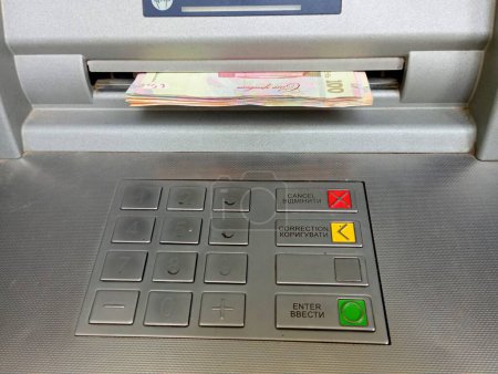Withdrawing money from an ATM. The photo shows cash as it looks from the money-dispensing window and the ATM keyboard. The topic of money and the work of the banking system.