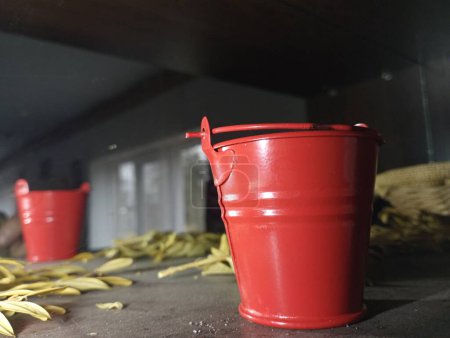 Photo for A small red bucket on a shelf with dry grass is reflected in the mirror behind. Fire equipment for transferring liquid. - Royalty Free Image