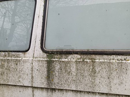 Foto de El viejo coche blanco está cubierto de musgo verde y liquen. El cuerpo podrido del coche está parado en el patio.. - Imagen libre de derechos