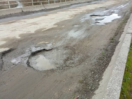 Huge potholes on the bridge in the asphalt road surface. Very bad road across the river. Road and road surface problems. Topics of transport and the field of road maintenance.