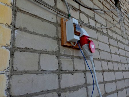 Plugged in mains charger and attached electrical outlet on a white brick wall. Charger for a car with package type fuses.