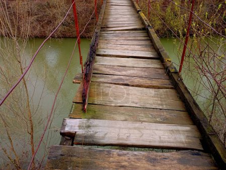 Alte Holzbrücke mit kaputten und morschen Brettern unter dem Fuß über den Fluss. Gefährliche Fußgängerbrücke ans gegenüberliegende Ufer des Flusses.