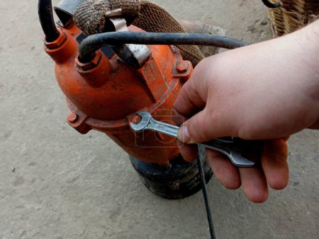 In the photo, a human hand unscrews a water pump with a wrench for repair and diagnosis. Independent repair of plumbing equipment.
