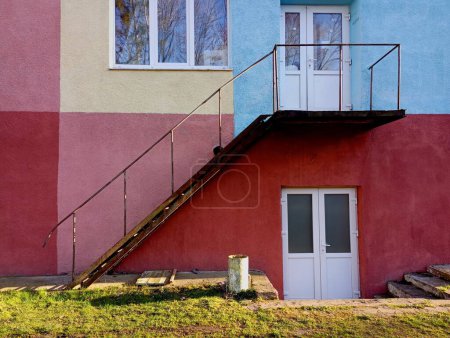 The wall is painted in different bright colors along which a metal ladder climbs to the second floor. Beautiful architecture with windows and doors. Entrance to the premises and windows on a brightly painted wall.