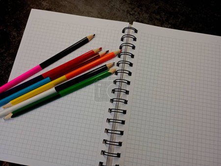 Photo for A set of colored pencils lie on a page of a notebook in a mathematical cell. Objects for creating drawings and sketches. The subject of art and drawing with colored pencils. - Royalty Free Image