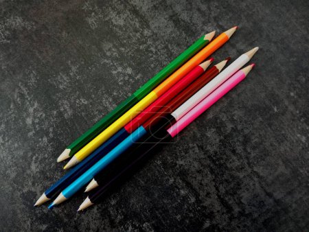 Eine Gruppe Bleistifte auf dunklem Betongrund ausgelegt. Buntstifte mit unterschiedlichen Farben auf beiden Seiten. Kunstgegenstände. Doppelseitige Bleistifte mit unterschiedlichen Farben von Graphit