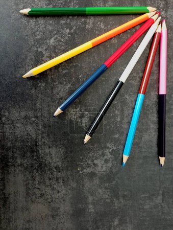 Auf grauem Betongrund sind in der rechten oberen Ecke Bleistifte in Form von Sonnenstrahlen ausgelegt. Bunte Holzstifte auf dunklem Hintergrund. Schreibwaren und Artikel für Studium und Kunst.