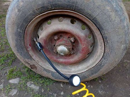 Foto de Bombeo de aire en la rueda con un pequeño compresor de coche. El neumático viejo en el remolque al tractor se infla con la ayuda de un compresor. - Imagen libre de derechos