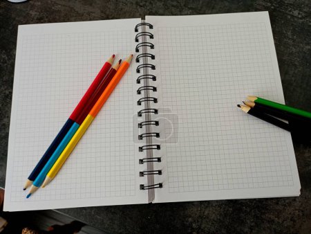 Photo for On the pages of the math notebook, colored pencils are arranged in a cell for drawing and art. Subjects of education and teaching of art. - Royalty Free Image