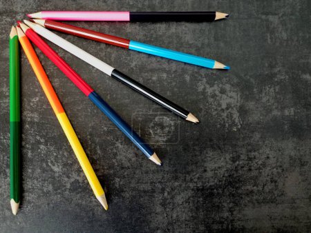 In der Ecke des Fotos vor dunklem Betongrund sind doppelseitige Bleistifte in verschiedenen Farben ausgelegt. Das Thema Zeichnung und Kunst.