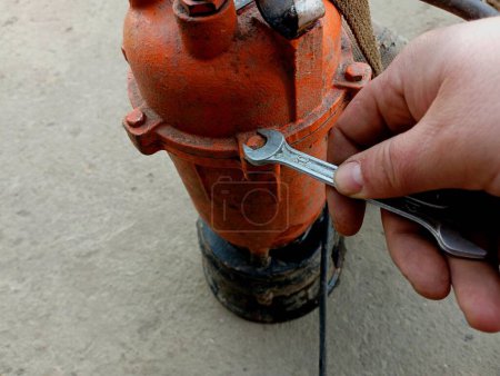 Reparatur einer Hydraulikpumpe zum Abpumpen von Wasser. Mann repariert orangefarbene Wasserpumpe mit Schraubenschlüssel.