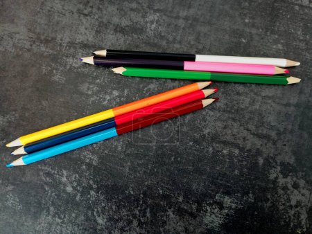 Téléchargez les photos : Les crayons bicolores de couleur divisés en trois groupes en deux groupes reposent sur un fond de béton foncé. Le sujet de l'éducation dans le domaine de l'art. - en image libre de droit