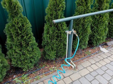 Comunicaciones alineadas para suministrar presión de aire con un compresor en el patio contra el fondo de árboles verdes que crecen uno al lado del otro y cubren la valla de metal verde detrás de ellos.
