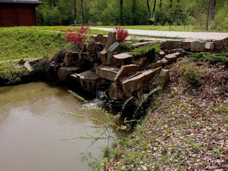 A beautiful stone dam with an artificial waterfall in the park with decorative trees and plants planted between the stones. Beautiful landscape design.