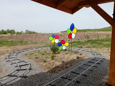The track of the children's railway attraction makes a U-turn around artificial flowers with multi-colored plastic petals. Beautiful landscape design in an amusement park for children.