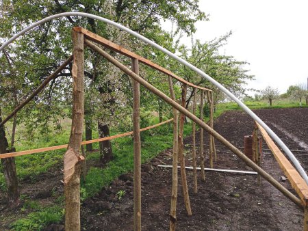 El marco del invernadero de materiales de madera improvisados y tuberías kesan en el jardín en primavera. Construyendo un invernadero con sus propias manos a partir de materiales a mano.