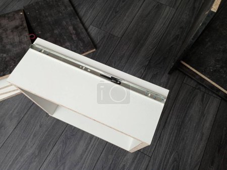 Eine weiße Schublade auf dem Boden während der Montage und Montage von ausziehbaren Verschlüssen. Einbau von Schubladenverschlüssen. Sammlung von Möbeln mit Schubladen.