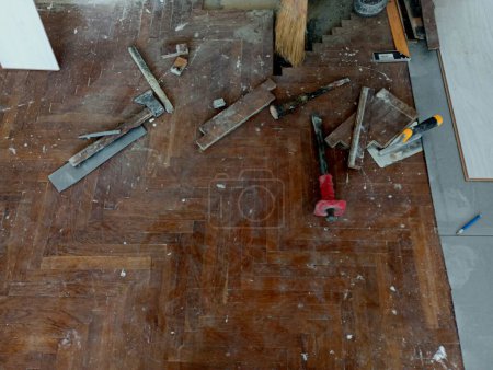 Der Parkettboden wird abgebaut, auf dem Handwerkzeuge verstreut sind. Der Prozess der Reparatur eines Parkettbodens. Reparatur und Werkzeuge für ihre Umsetzung.