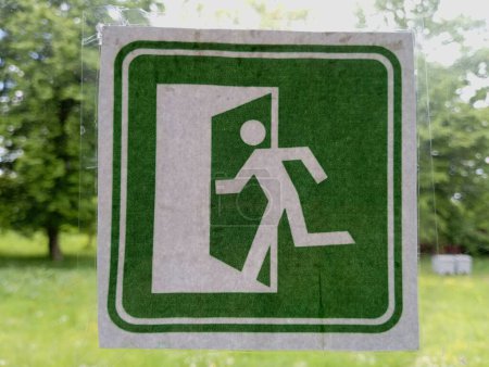 An emergency exit sign in case of fire or emergency is pasted on the door glass. The emergency exit sign is green.