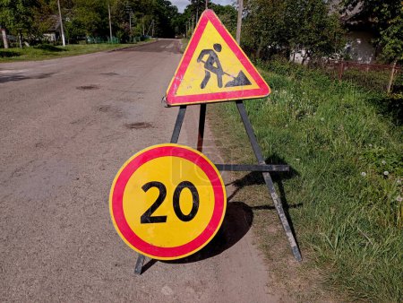 Photo for Road surface repair is underway on a rural road on which there are two signs, one emergency road repair sign and a speed limit sign up to 20 km/h. The topic of road repair. - Royalty Free Image