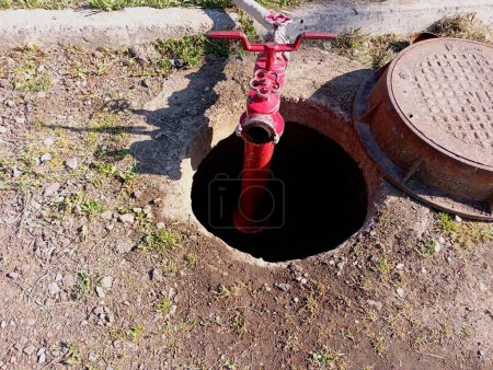 En la escotilla del pozo de aguas residuales, se instala una boca de incendios roja en la columna. El tema del suministro de agua en la ciudad y la seguridad contra incendios.