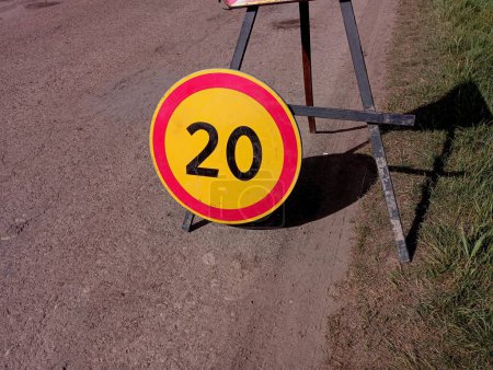 Téléchargez les photos : Un panneau de limitation de vitesse ne dépassant pas 20 km se trouve sur le côté du tronçon routier où des réparations sont effectuées. Panneau rond de 20 sur fond jaune entouré d'un cercle rouge. - en image libre de droit