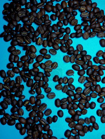 Black roasted coffee beans on a blue background scattered in a chaotic order. The topic of drinks and coffee shops.