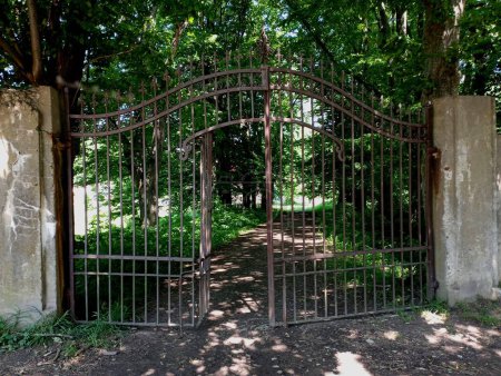 Photo for Ancient forged metal gate in the concrete wall of the park. Entrance to the park with a large iron gate. Closed gates at the entrance to a picturesque summer park. - Royalty Free Image