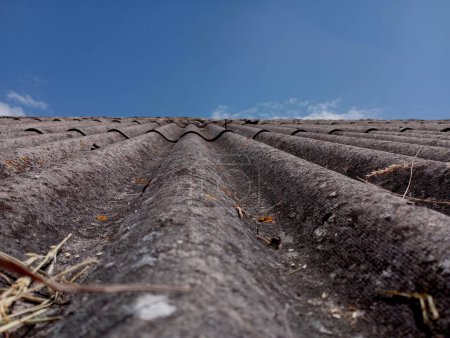 Ein Dach aus Asbestblech mit tiefen Bögen zur Wasserableitung vor dem Hintergrund des Himmels. Alte Schieferverkleidung des Hauses.