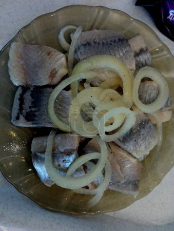 Pieces of delicious herring marinated in vinegar with onions are laid out on a transparent glass plate. Cooking fish and seafood dishes.