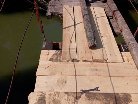 Der Prozess der Reparatur eines alten hölzernen Übergangs über einen Fluss. Auf dem Foto ist eine Holzkreuzung ein Reparaturwerkzeug, auf dem ein Schlüssel zum Lösen von Schrauben ruht. Reparatur der Fußgängerbrücke über den Fluss.
