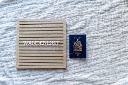 Foto de Wanderlust palabra en un tablero de madera beige con letras blancas con un pasaporte canadiense - Imagen libre de derechos