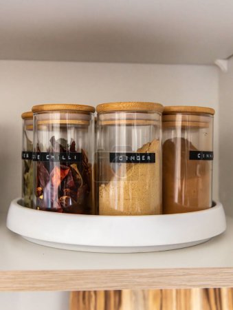 Photo for Neatly organized labeled food pantry in a home kitchen with spices in glass wooden spice jars - Royalty Free Image