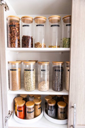 Photo for Neatly organized labeled food pantry in a home kitchen with spices in glass wooden spice jars - Royalty Free Image