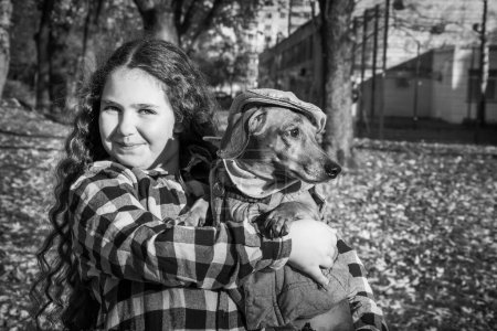 Photo for In the autumn park, a girl holds a dachshund dog in her arms.Black and white photo. - Royalty Free Image