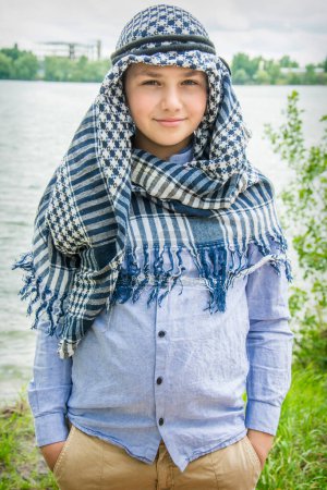 Téléchargez les photos : En été Dans la rivière pendant la journée, un beau garçon dans un arafatka, une écharpe arabe se tient debout sur la route. - en image libre de droit