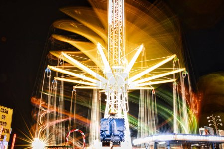 Foto de Larga exposición de un carrusel brillantemente iluminado por la noche, capturando el desenfoque de movimiento de las luces giratorias en una feria. - Imagen libre de derechos