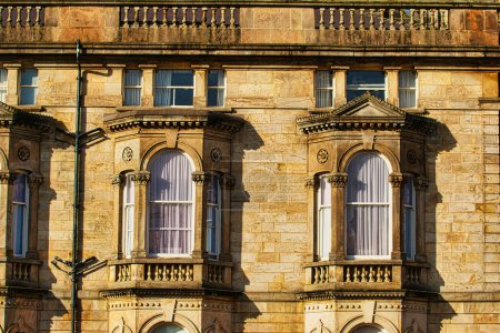 Nahaufnahme einer klassischen Sandsteinfassade mit kunstvollen Fenstern und architektonischen Details im warmen Sonnenlicht in Harrogate, England.